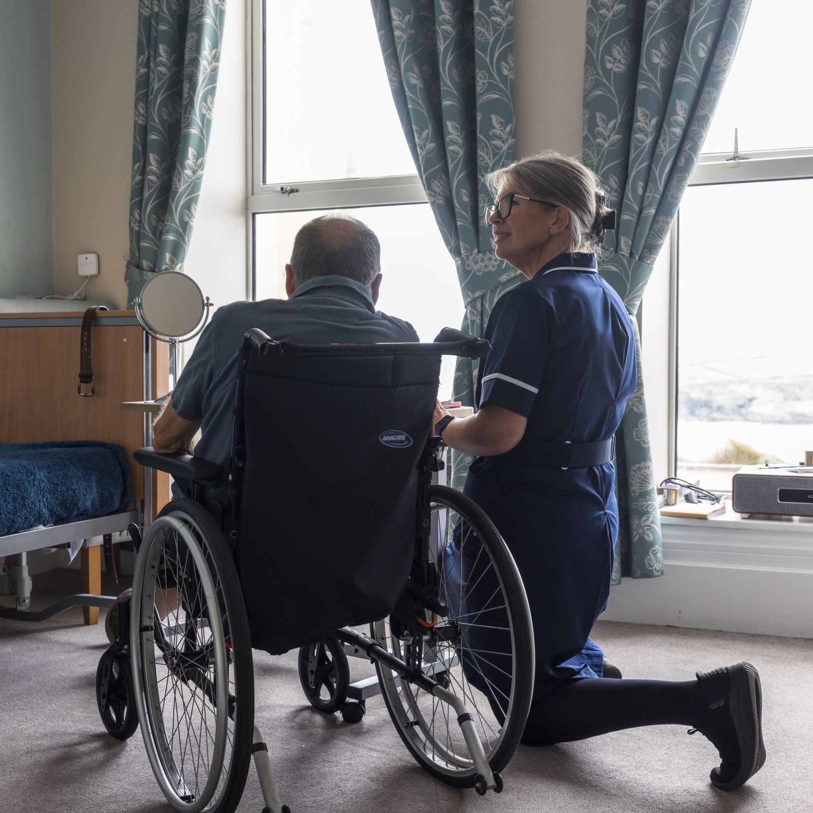 A female nurse kneeling down to a man in a wheelchair