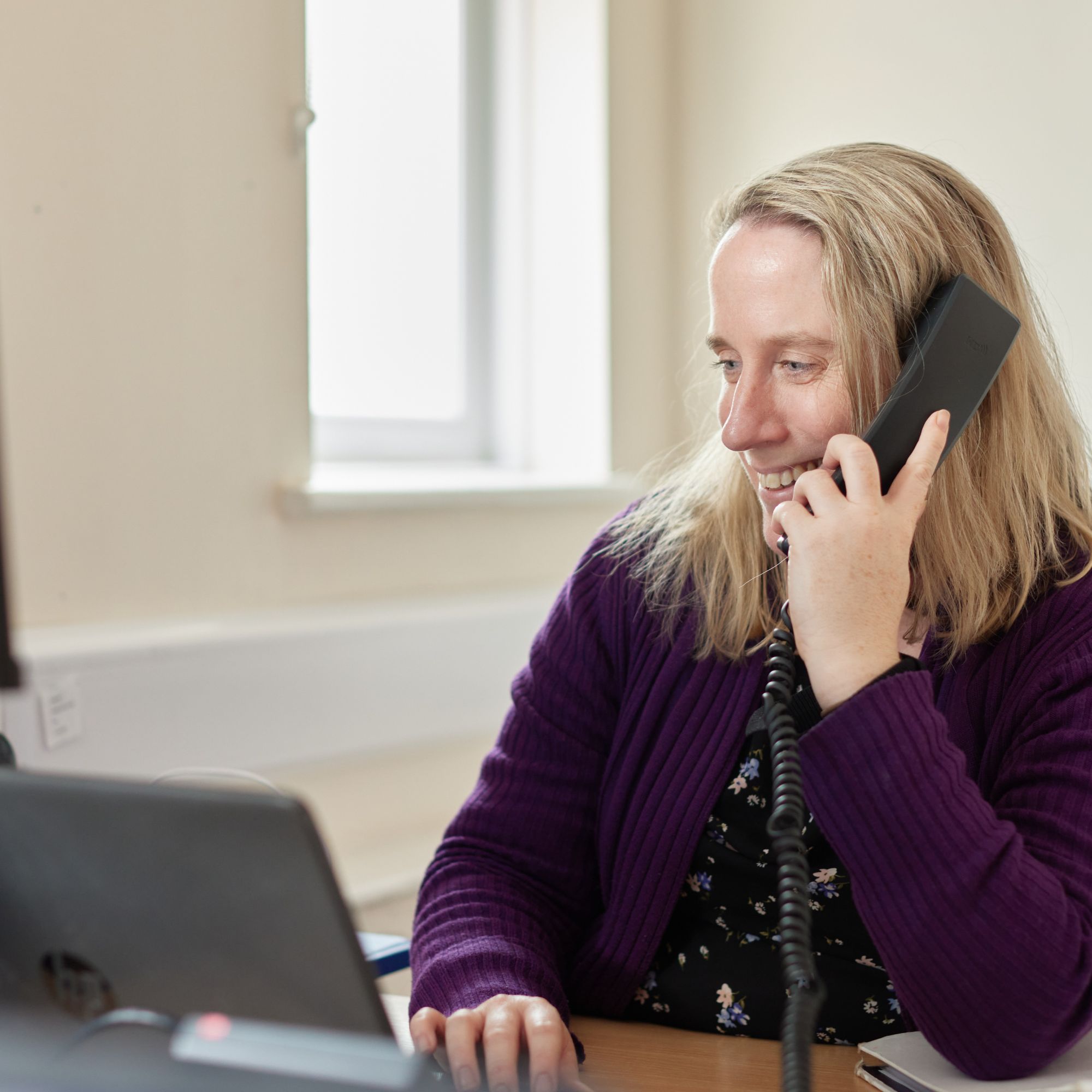 A woman on the phone smiling whilst using a laptop