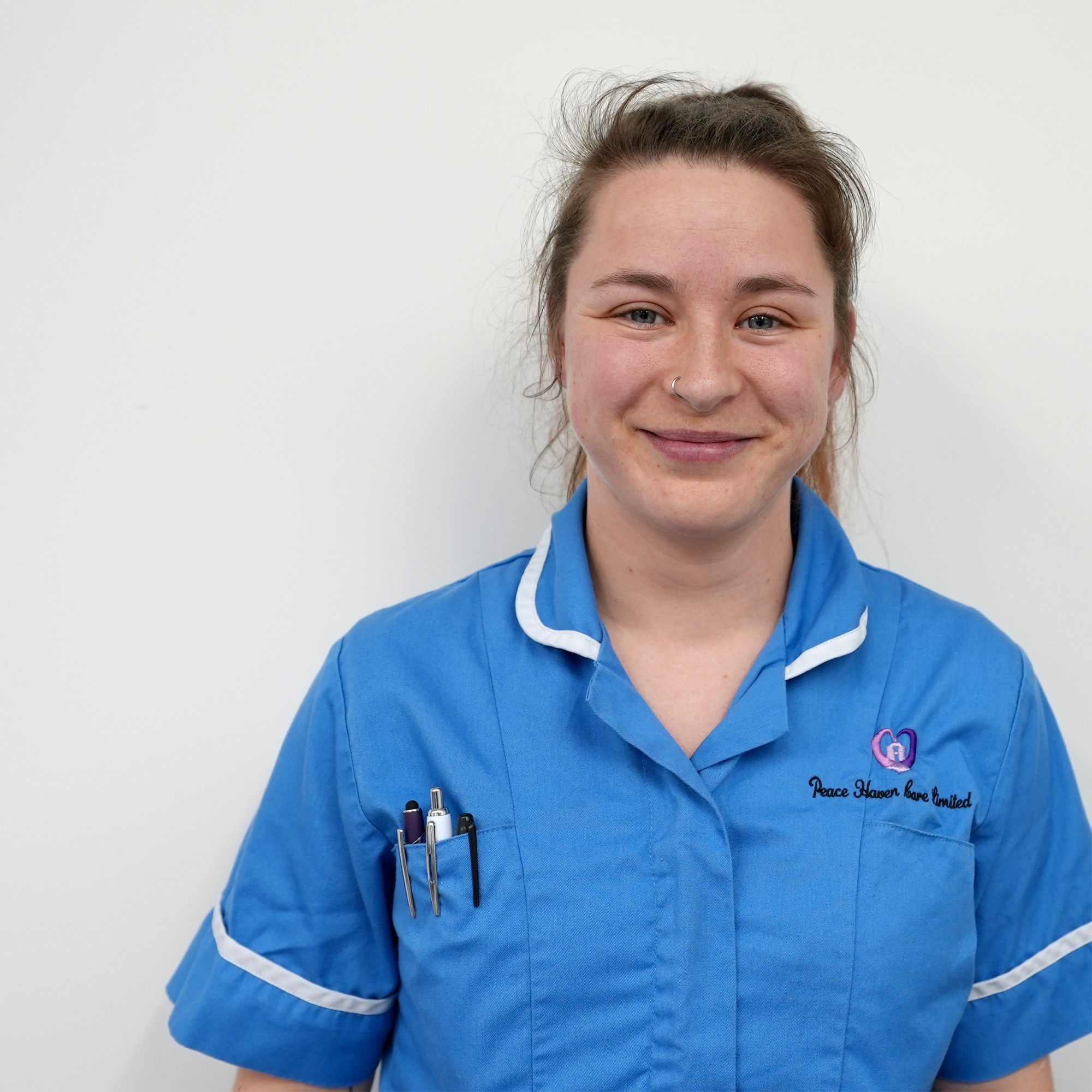A young female home care worker in uniform smiling at the camera